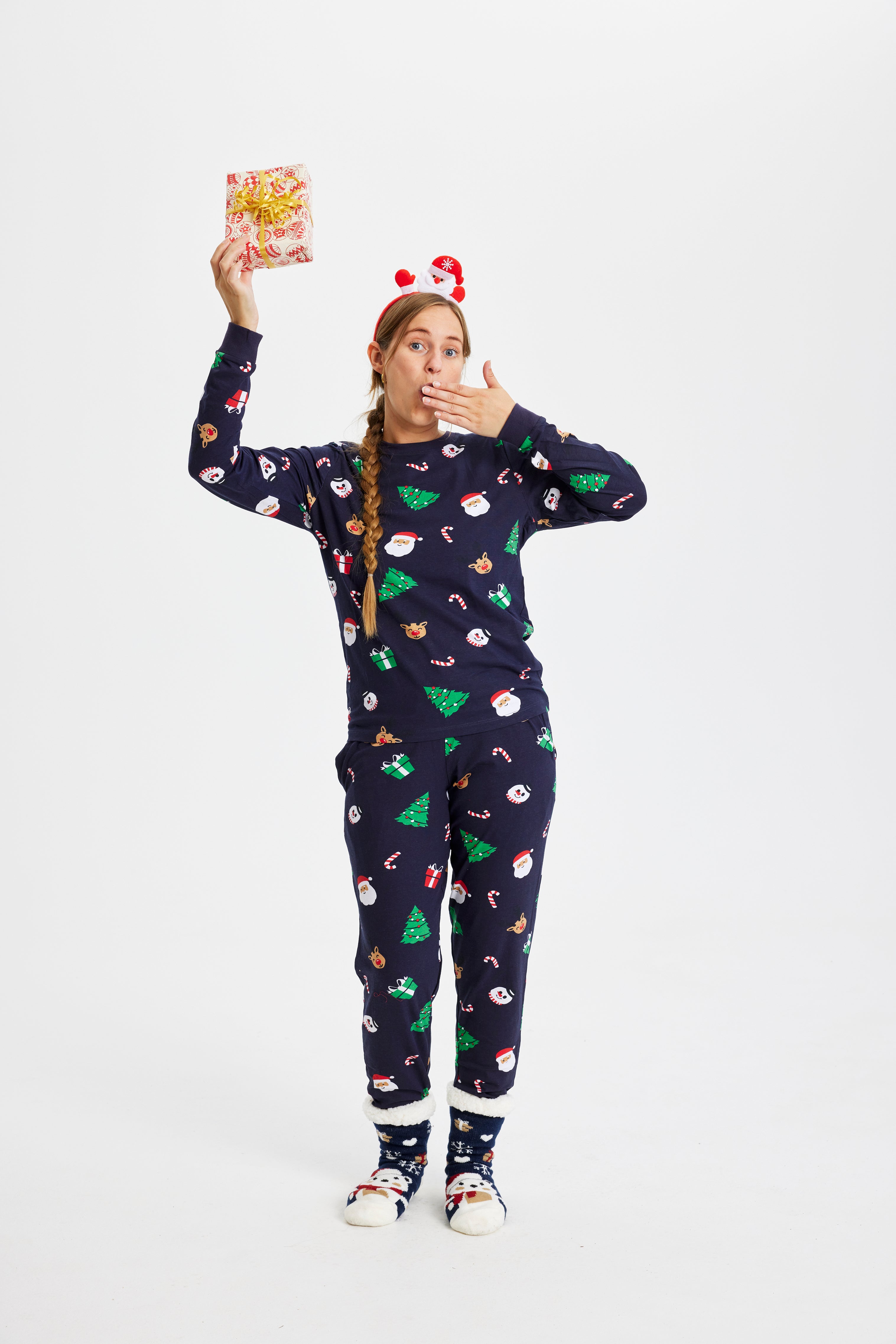 Une femme posant avec un cadeau portant un pyjama de Noël avec des arbres de Noël.